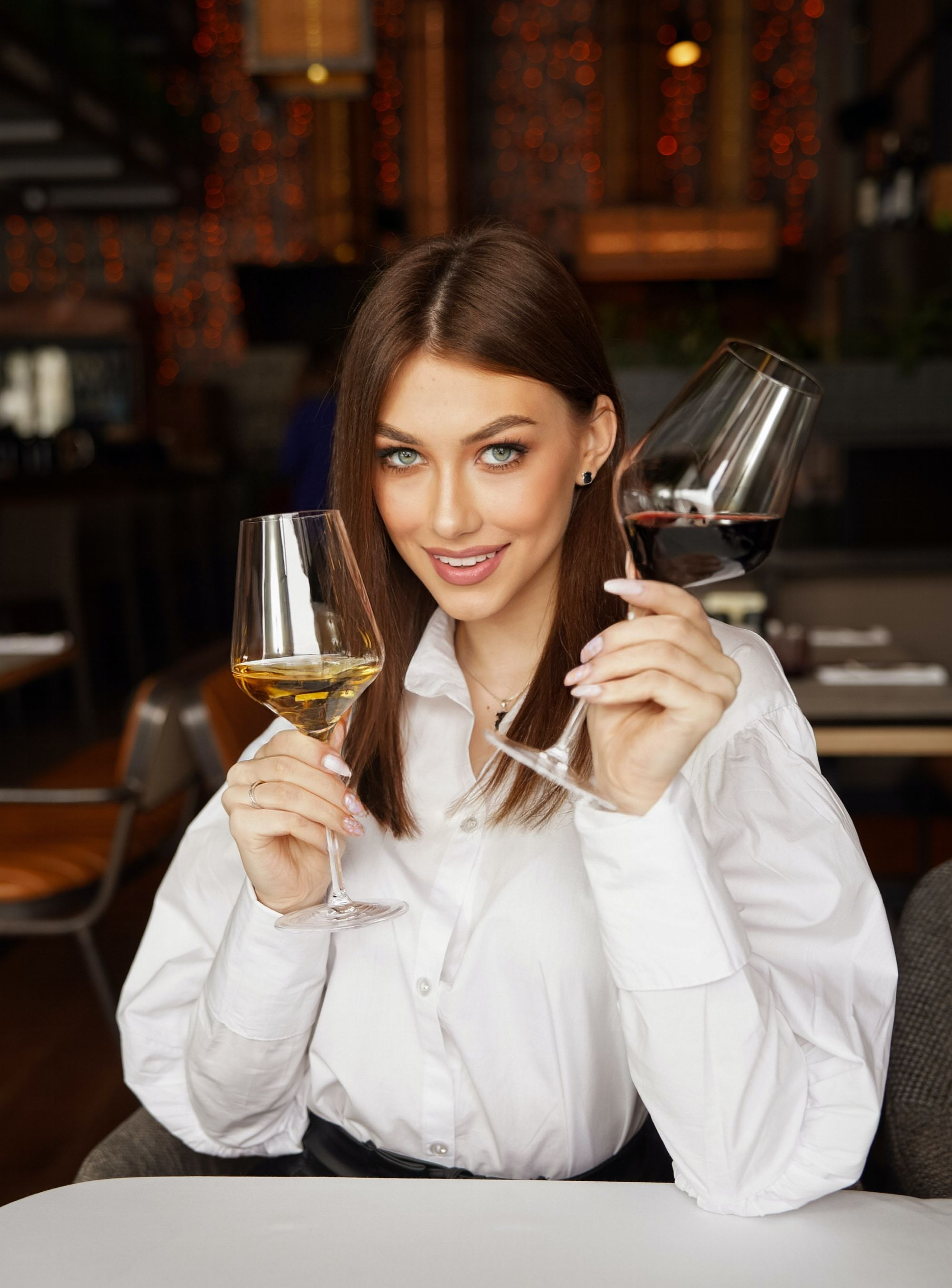 A person holding a bottle of red wine and a glass of white wine